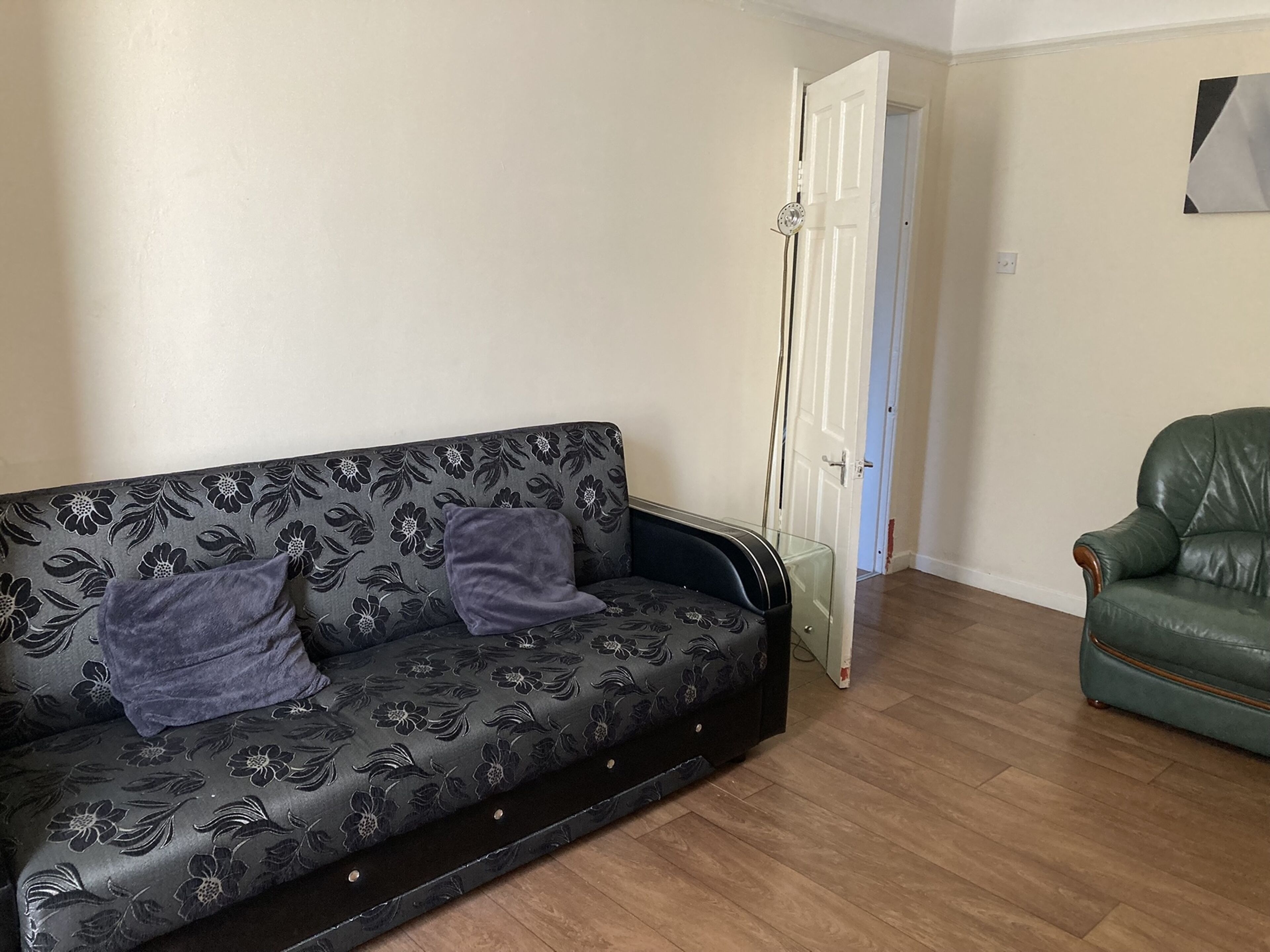 A living room with a patterned sofa, a green leather armchair, and a door leading to another room.
