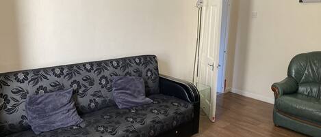 A living room with a patterned sofa, a green leather armchair, and a door leading to another room.
