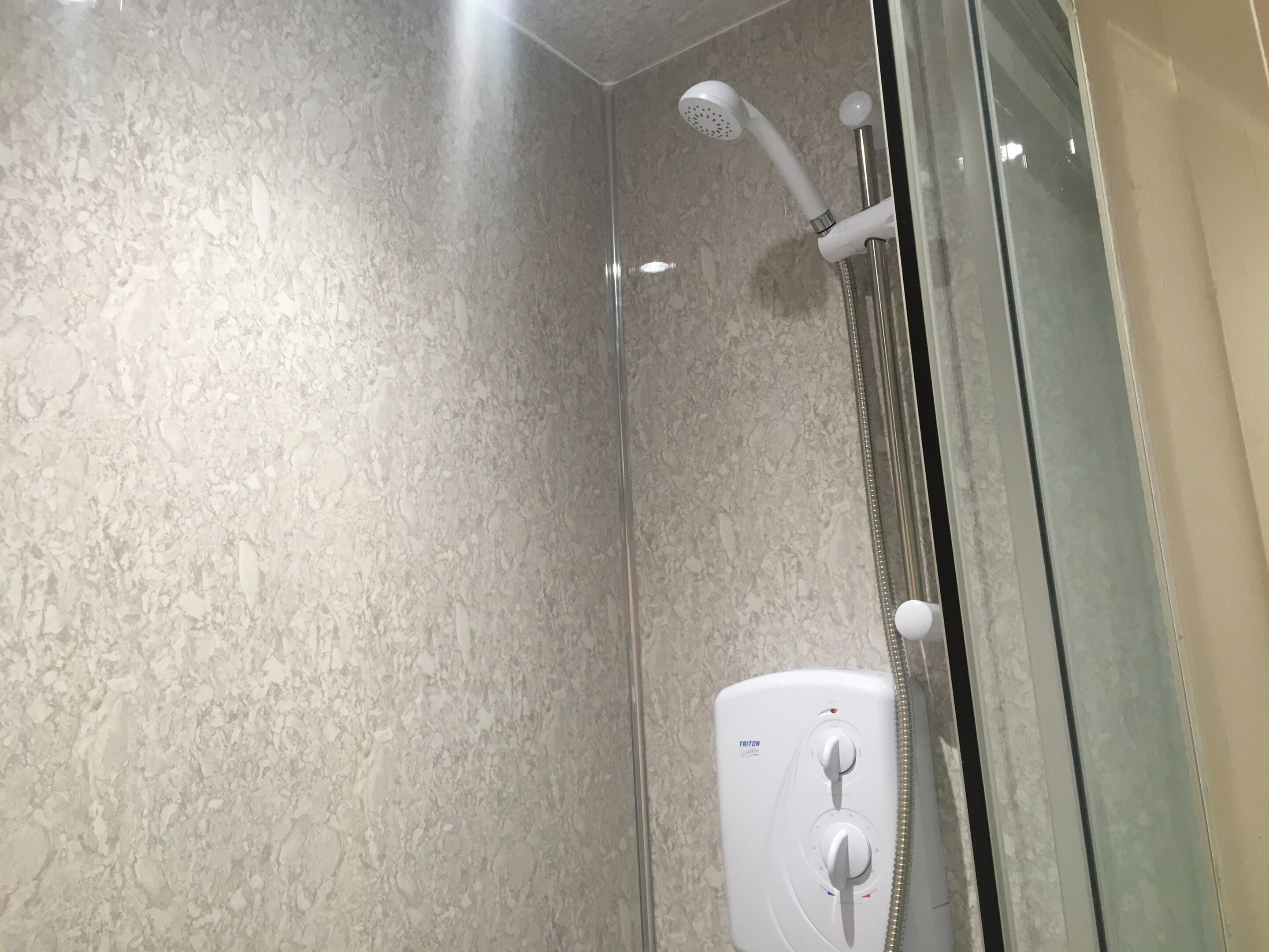 A shower with a handheld showerhead and a wall-mounted control panel.