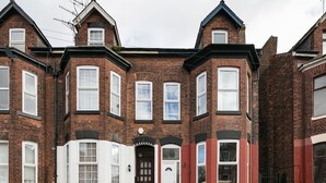 A two-story brick house with a bay window, a white front door, and a small porch. - 6 Bedroom Chorlton Townhouse (Manchester)