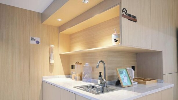 A modern kitchen with a built-in sink, wooden cabinetry, and a countertop with various kitchen items. - Crystal Haolaideng Hotel (Dehua)