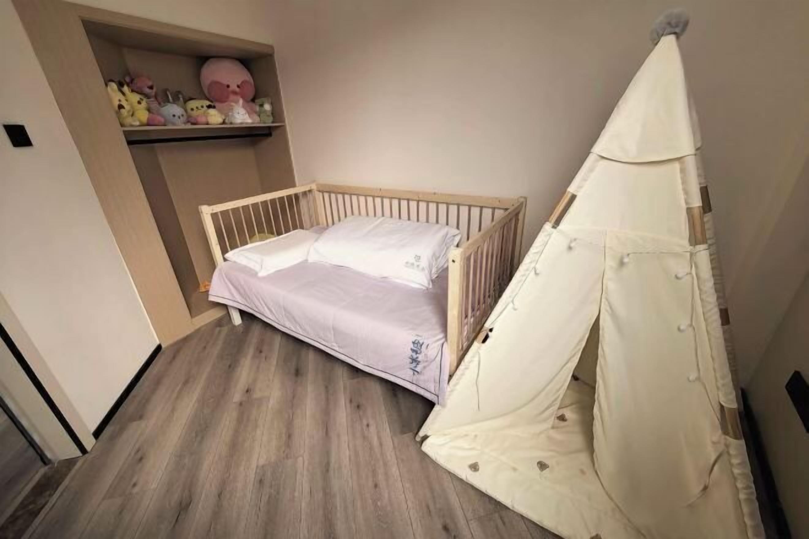 A small, single-bed room with a wooden frame, a white canopy, and a shelf with plush toys.