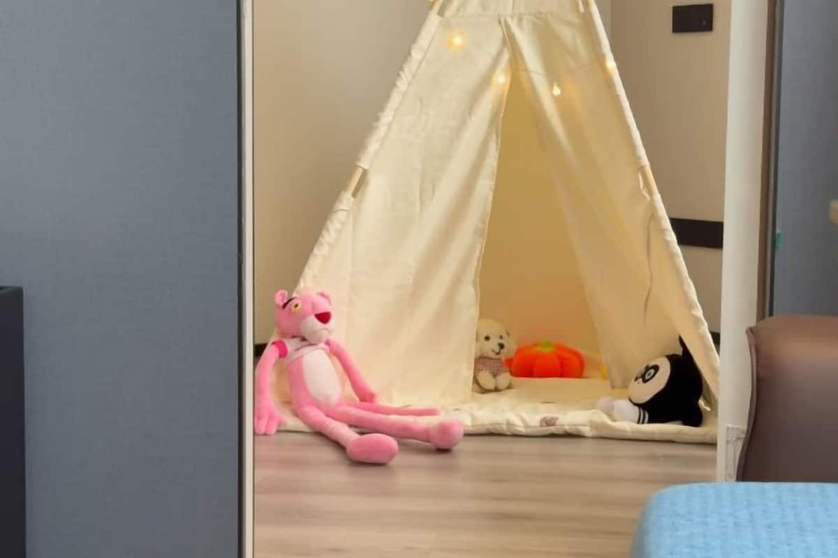 Une pièce avec une structure ressemblant à une tente, un jouet en peluche rose, un ours en peluche blanc et un jouet noir et blanc.