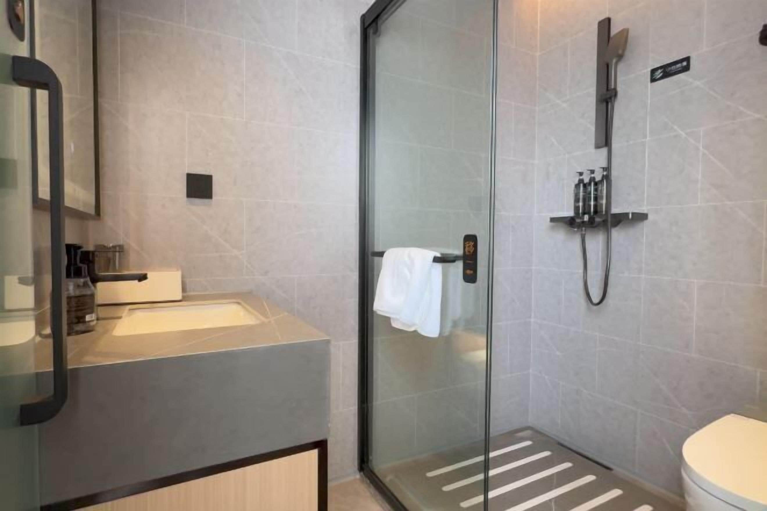 Ein modernes Badezimmer mit Duschkabine aus Glas, einem Waschbecken mit Handtuchhalter und einer Toilette.