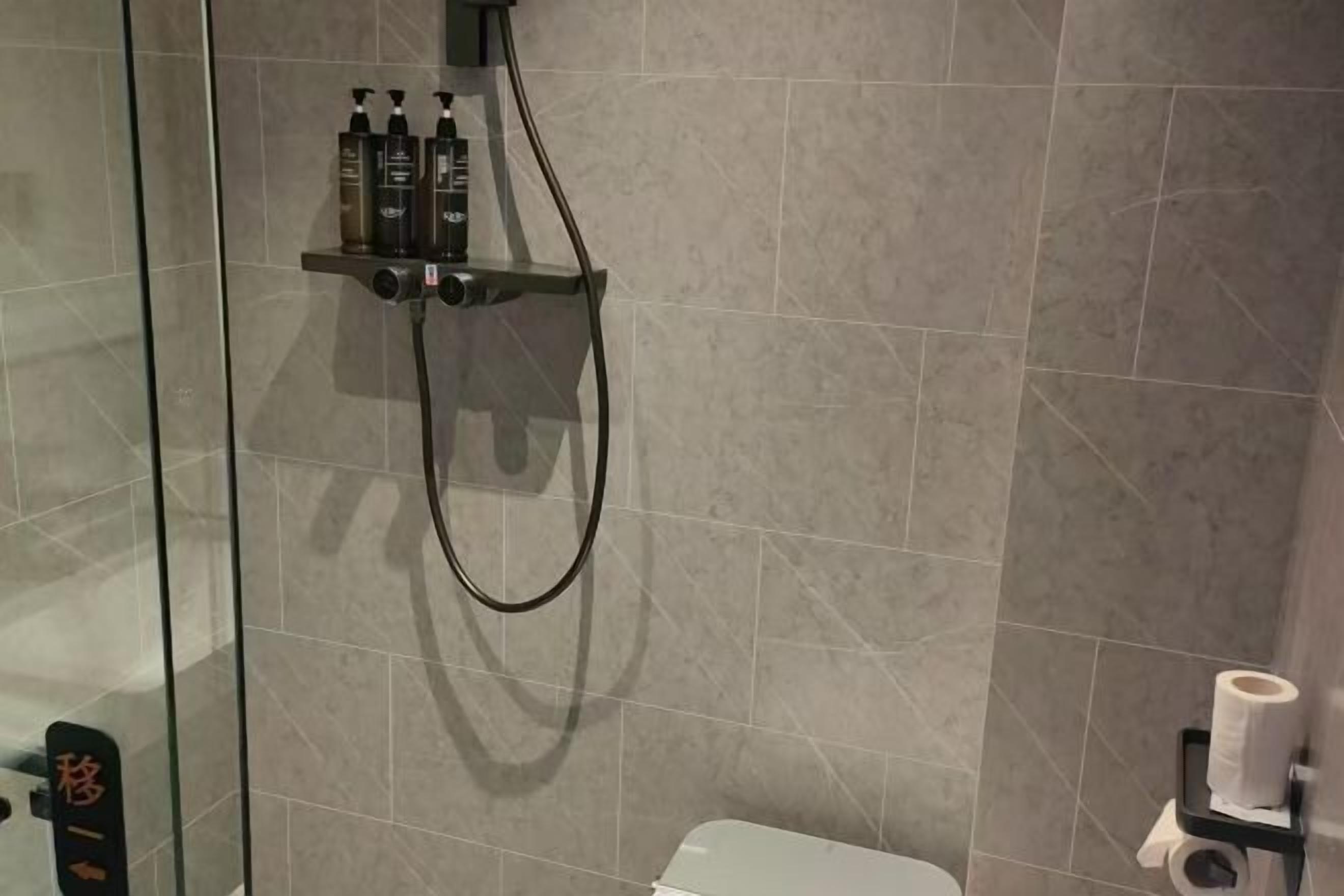 Ein Duschbereich mit Glastrennwand, Handbrause und Ablage für Toilettenartikel.