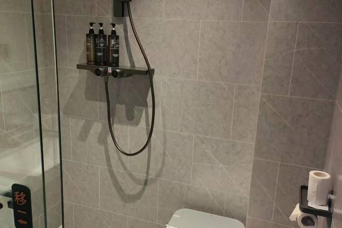 Un espace douche doté d’une paroi en verre, d’un pommeau de douche à main et d’une étagère pour les articles de toilette.