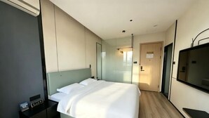 A modern hotel room with a large bed, a bedside table, a TV, and a mirror. - Crystal Haolaideng Hotel (Dehua)