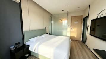 A modern hotel room with a large bed, a bedside table, a TV, and a mirror.