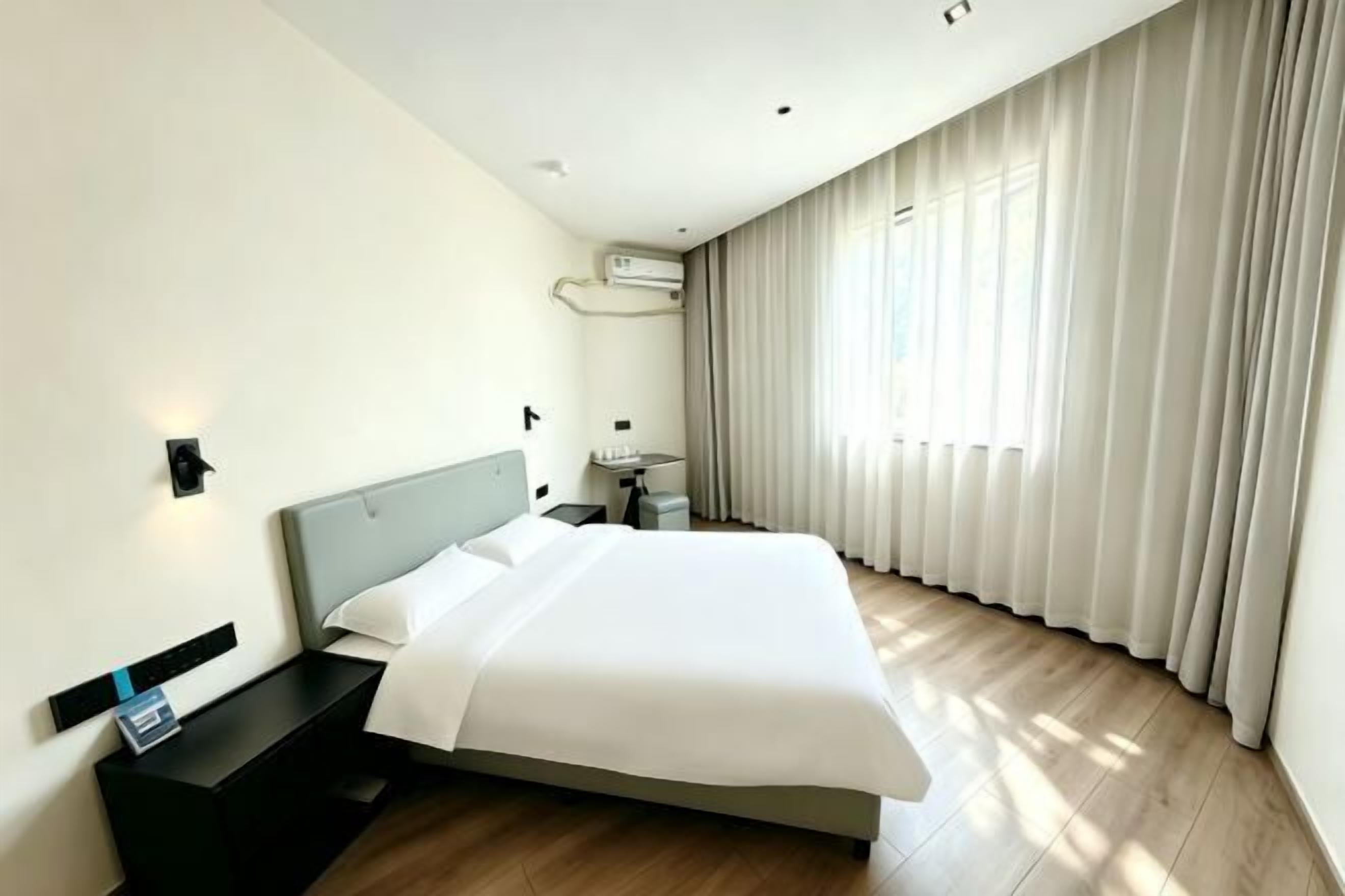 A modern hotel room with a large bed, bedside tables, a nightstand, a desk, and a window with curtains.