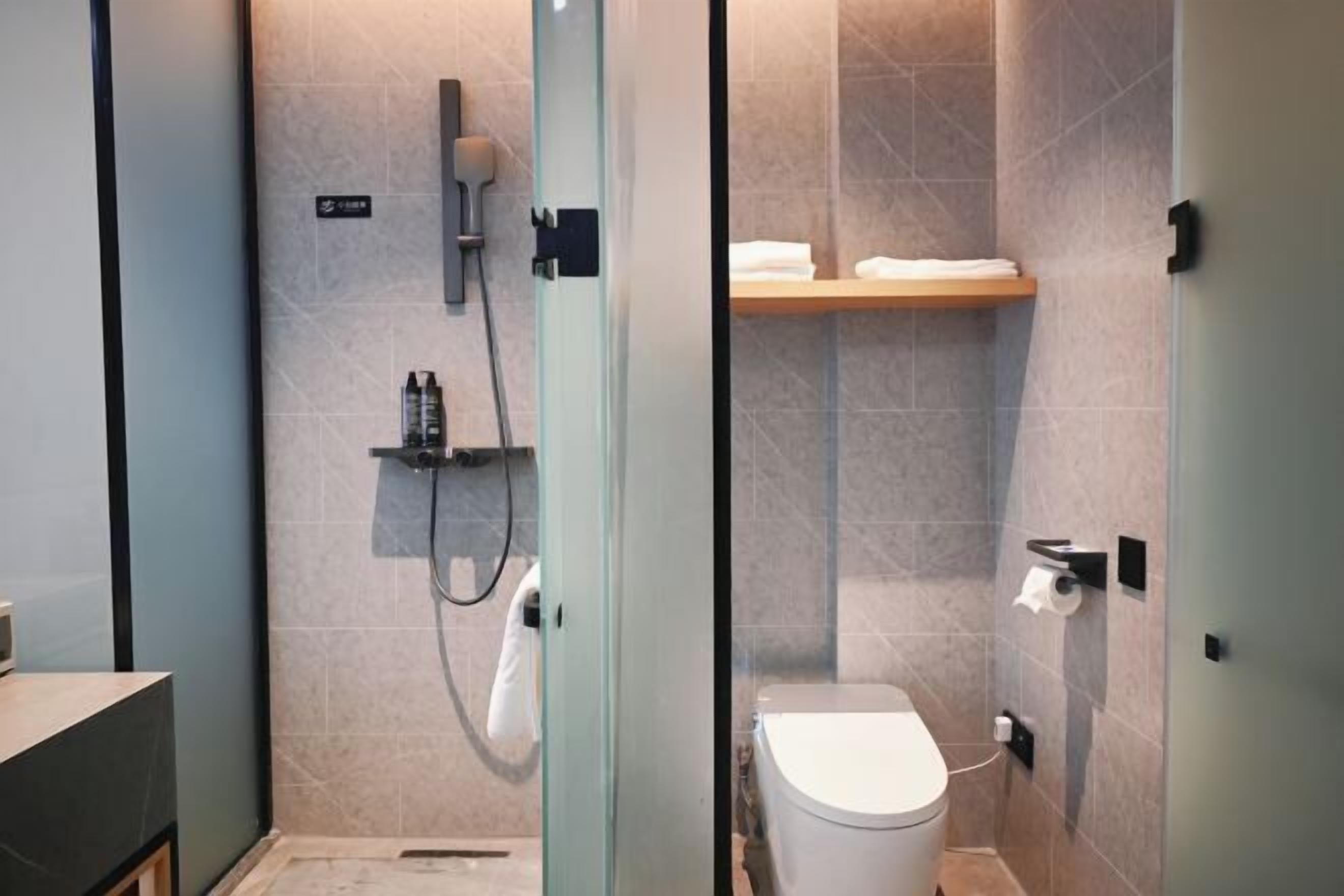Ein modernes Badezimmer mit einer Duschkabine aus Glas, einer Toilette und einem Ablagefach mit Handtüchern.