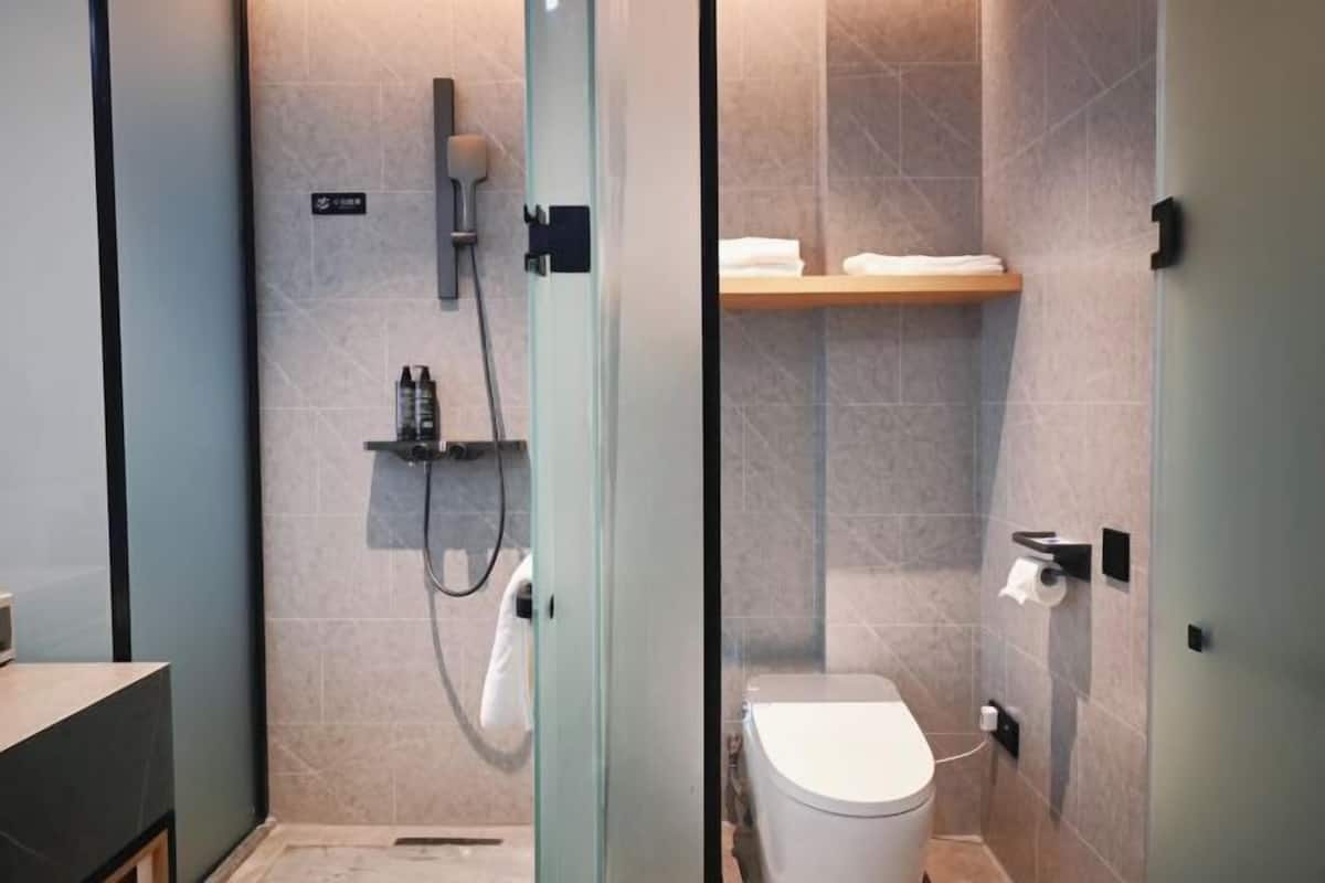 Une salle de bain moderne avec une douche à l’italienne en verre, des toilettes et une étagère avec des serviettes.
