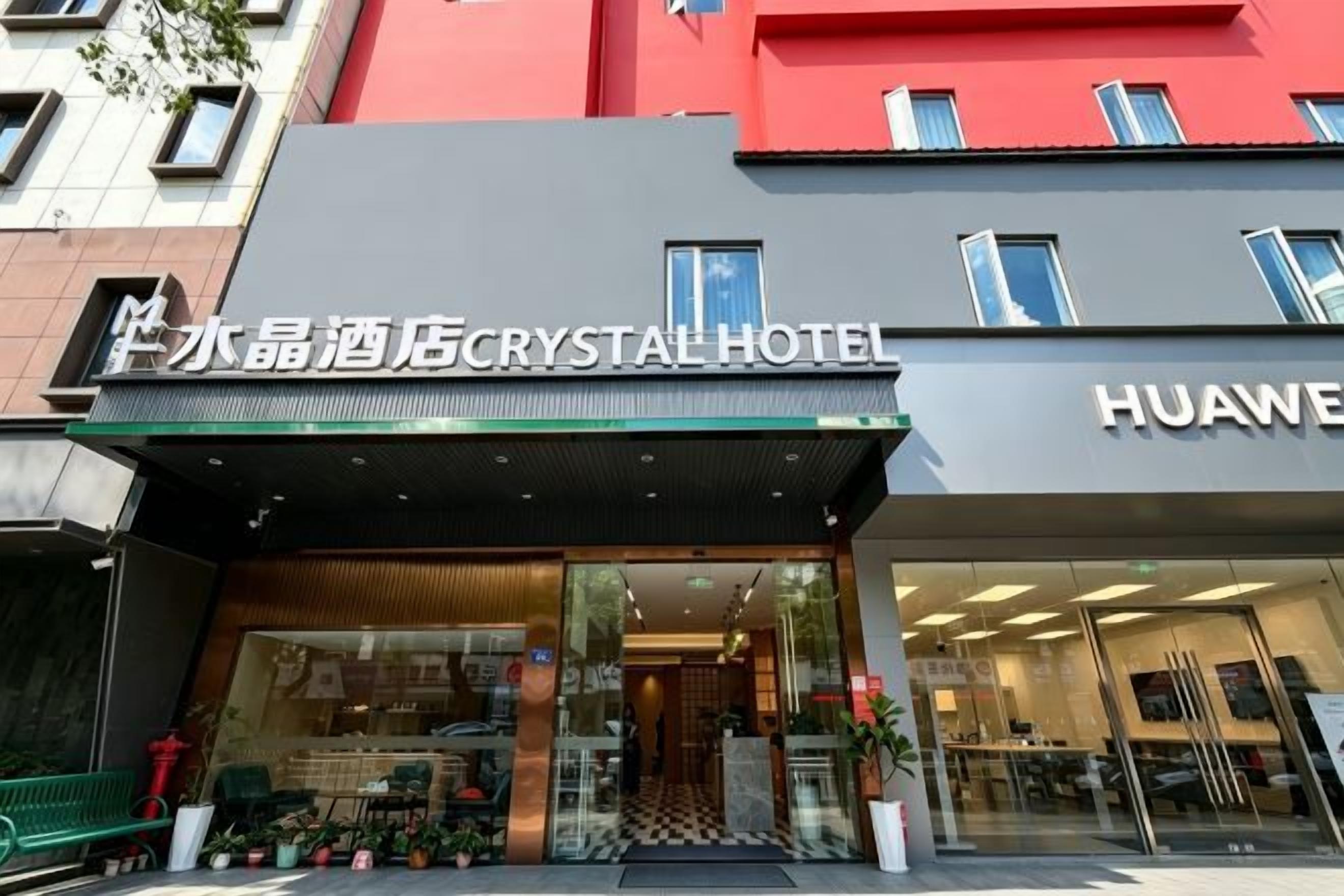 Entrada de un hotel con un letrero que dice 'Crystal Hotel' y una tienda 'Huawei' al otro lado de la calle.