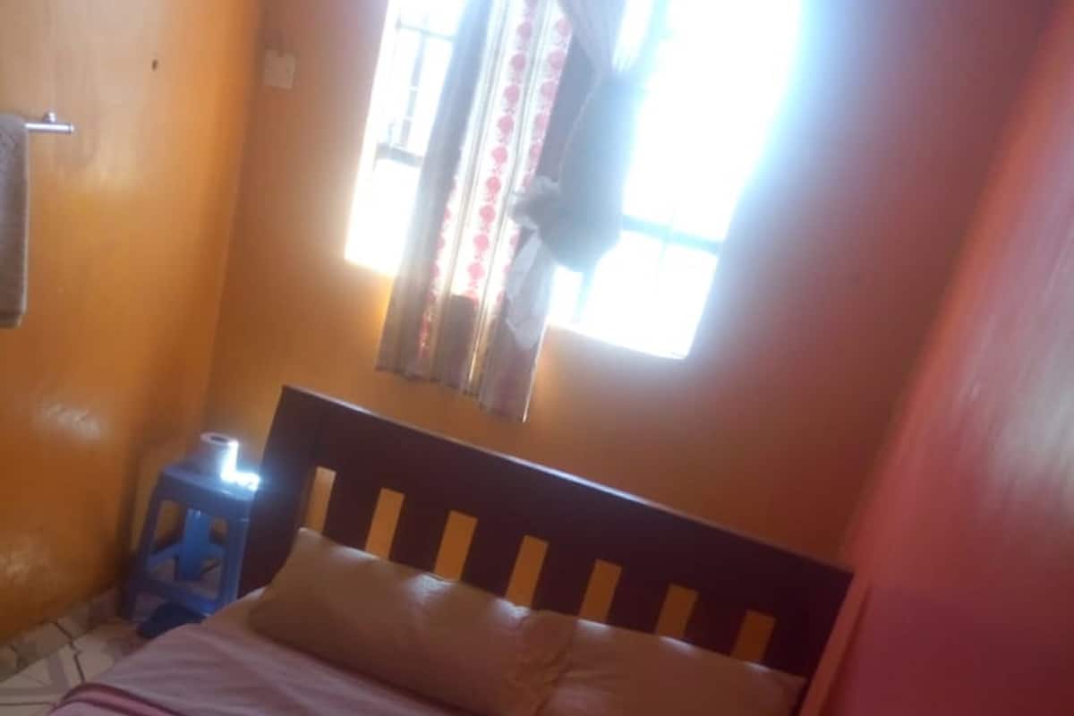 A bedroom with a bed, a window with curtains, and a blue stool.