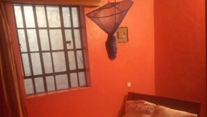 A bedroom with a bed, a window with bars, and a hanging mosquito net. - Jambo Guest House (Nairobi)