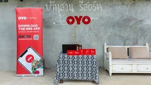 Habitación de hotel con un gran anuncio de la aplicación OYO, una pequeña mesa con un teléfono inteligente y un sofá blanco con cojines.