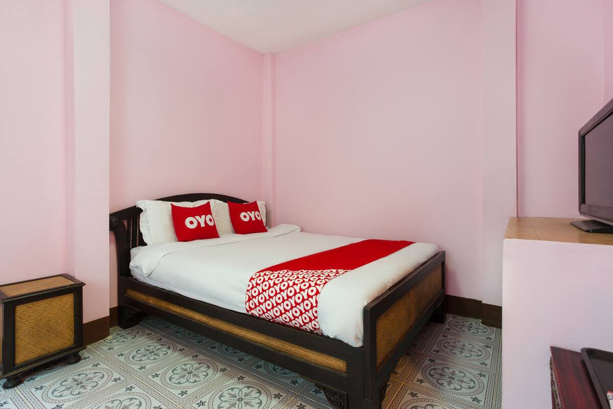 Una cama individual con estructura de madera, ropa de cama blanca y almohadas rojas y blancas.