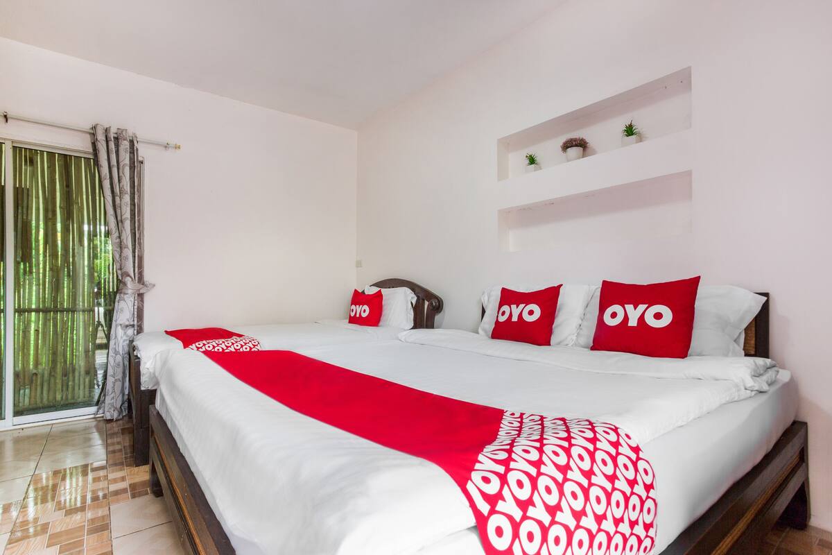 Habitación de hotel con una cama grande, una manta de diseño rojo y blanco, y tres almohadas rojas con la palabra 'OYO' escrita.