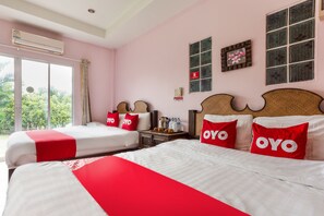 A hotel room with two beds, each with red and white bedding and pillows, a wooden headboard, a nightstand with a coffee pot, and a window with a view of greenery. - OYO 749 Baan Suan Resort (San Kamphaeng)
