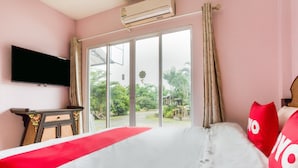 Habitación de hotel con una cama grande, un televisor de pantalla plana en la pared y un ventanal corredero que da a un jardín.
