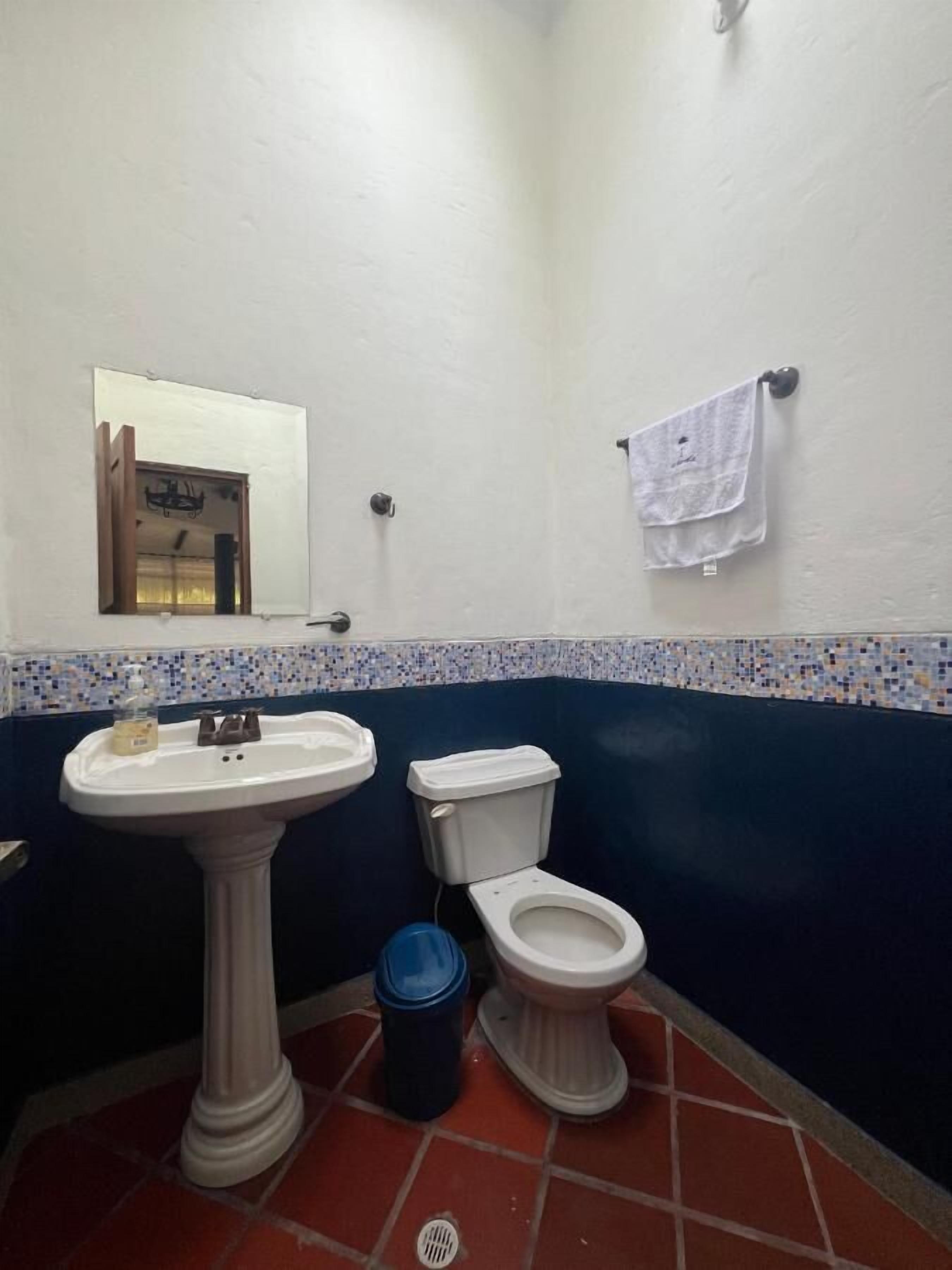 Un baño con lavamanos pedestal, inodoro y una ventana pequeña.