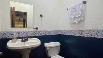 Un baño con lavamanos pedestal, inodoro y una ventana pequeña.