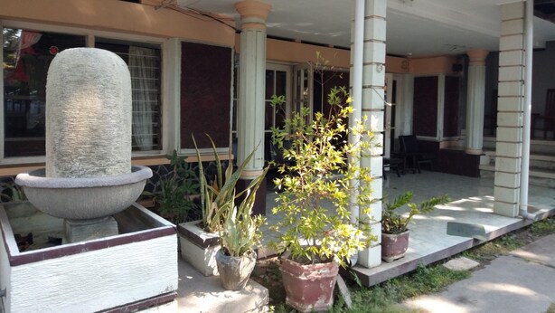 A covered outdoor area with a stone fountain, potted plants, and a seating area with chairs. - Duta Karya Hotel (Buleleng)