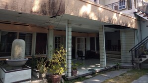 A two-story house with a covered porch, potted plants, and a stone fountain. - Duta Karya Hotel (Buleleng)