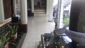 A hotel lobby with a fountain, tiled flooring, and potted plants. - Duta Karya Hotel (Buleleng)