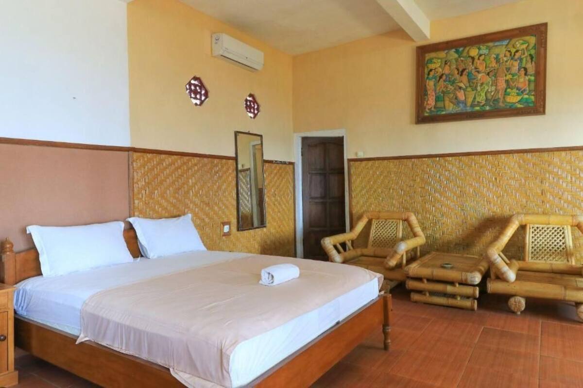Una habitación con cama, una silla, aire acondicionado de pared, una puerta y un cuadro.