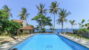 A rectangular swimming pool with a tiled edge, surrounded by palm trees and a view of the sea.