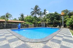 Relax by the clear blue pool surrounded by lush greenery and a geometric-patterned deck.