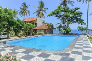 Uma piscina com deck ladrilhado, rodeada por palmeiras e um edifício com telhado telhado.