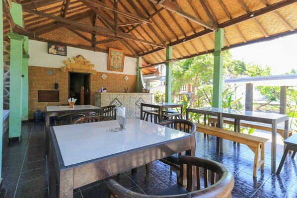 Restaurante com telhado de palha, mesas e cadeiras de madeira e vista para o verde lá fora.