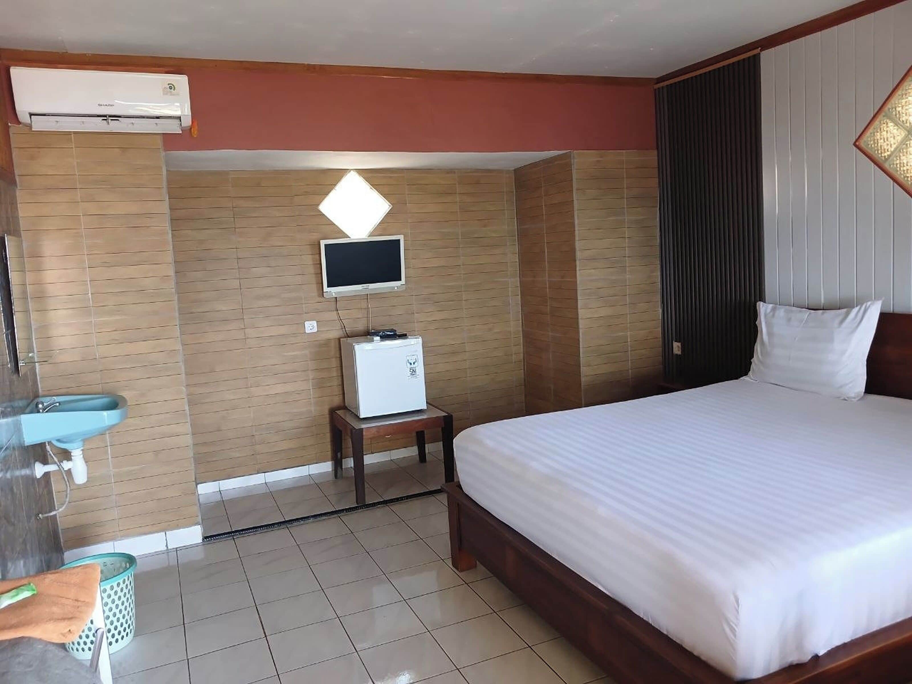 Una habitación de hotel con una cama, televisión, una mesita y un lavamanos.