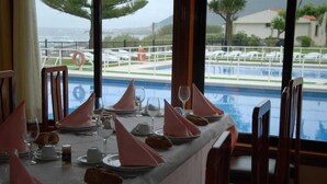 A dining table set for a meal with a view of a pool and beach in the background. - Hotel Restaurante Glasgow (Oia)