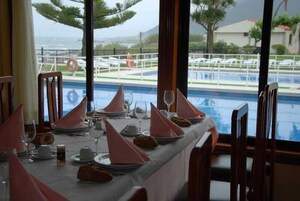 Mesa de comedor lista para una comida, con vista a una piscina y la playa al fondo.
