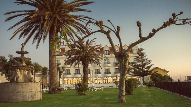 A hotel with a courtyard featuring palm trees, a fountain, and outdoor seating. - Hotel Restaurante Glasgow (Oia)