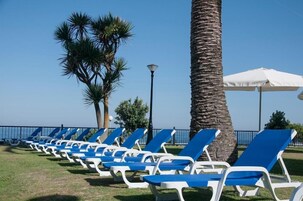 Una hilera de sillones azules y blancos alineados sobre una zona cubierta de césped, con una palmera y un farol.