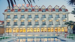 A hotel with multiple balconies, a swimming pool, and a well-lit facade. - Hotel Restaurante Glasgow (Oia)