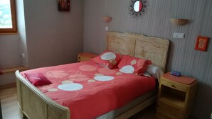 Un dormitorio con una cama de madera, una colcha estampada en rojo y blanco, dos mesitas de noche, un reloj de pared y un espejo decorativo.