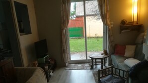 Una sala de estar con un sofá, una televisión, una mesita y un ventanal corredizo que da a un jardín.