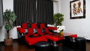 A living room with a red and black sofa, a glass coffee table, black ottomans, and a potted plant. - Wirton Dago Hotel (Bandung)