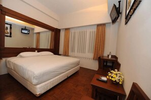 A hotel room with a large bed, a small table with a vase of flowers, a television, and a window with curtains. - Wirton Dago Hotel (Bandung)
