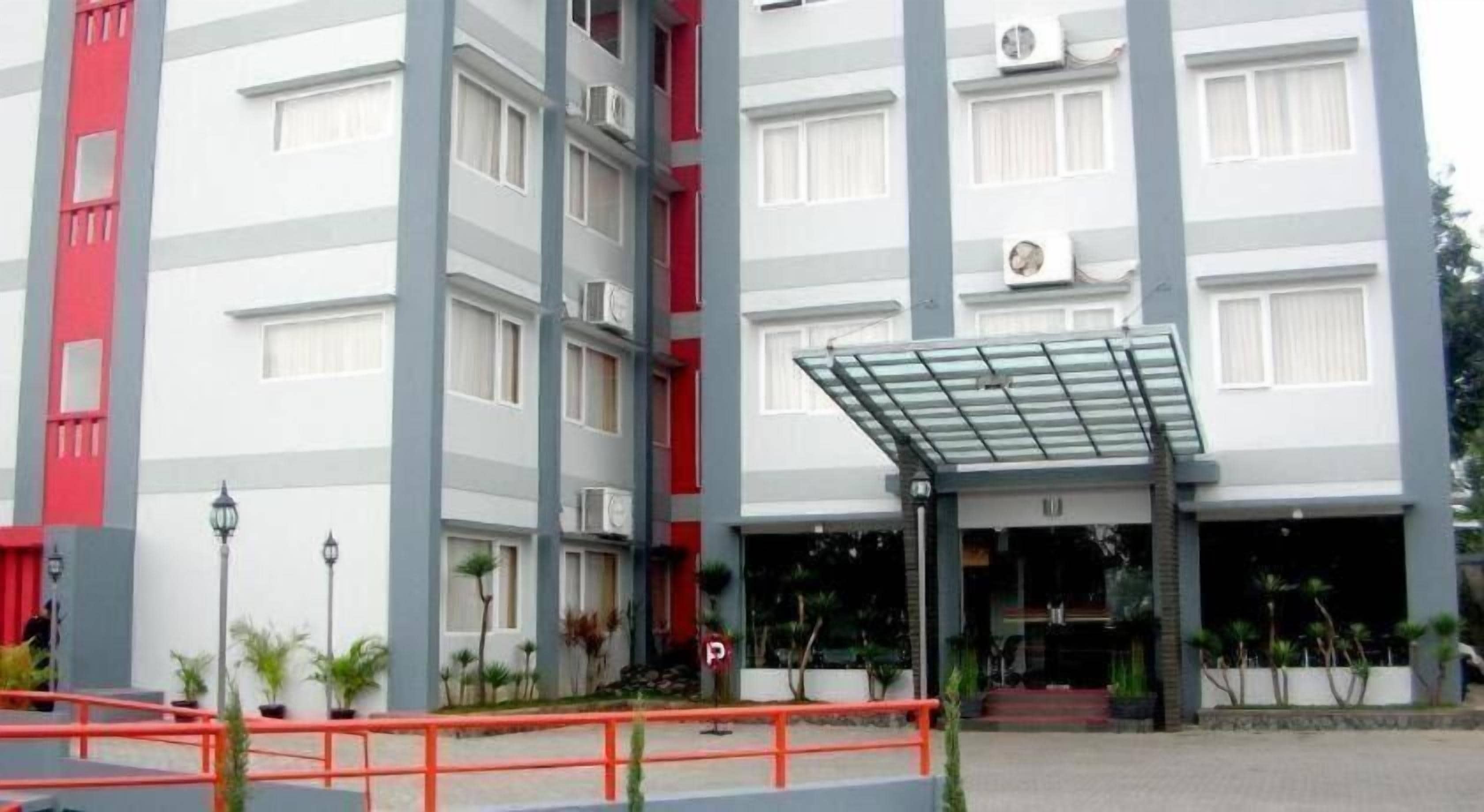 A multi-story building with a covered entrance, potted plants, and a red railing.