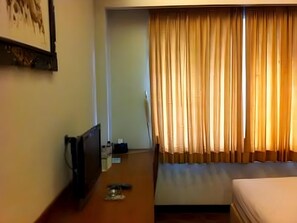 A hotel room with a bed, a desk with a computer, and a window with curtains. - Wirton Dago Hotel (Bandung)