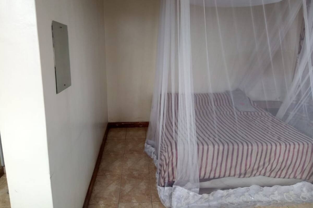 Un dormitorio con una cama bajo una mosquitera, suelo de baldosas y un enchufe en la pared.
