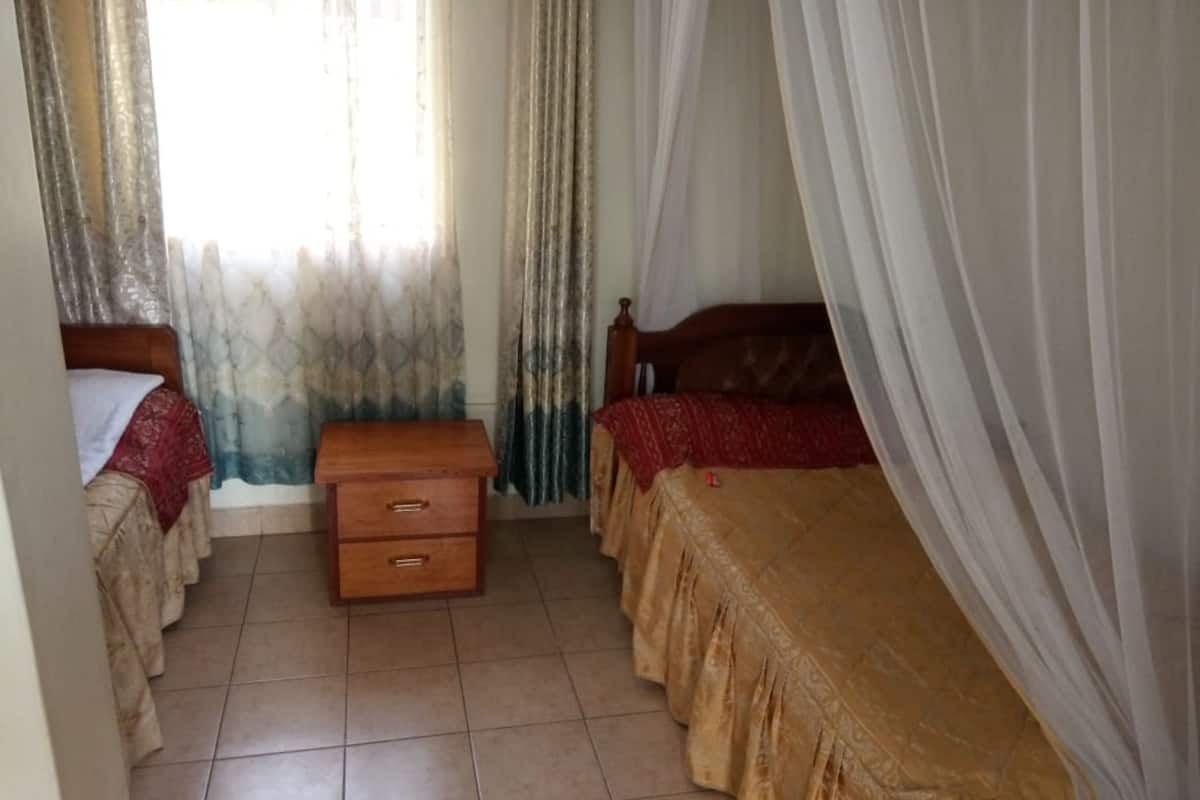 Un dormitorio con dos camas, una mesita de noche de madera y una ventana con cortinas.