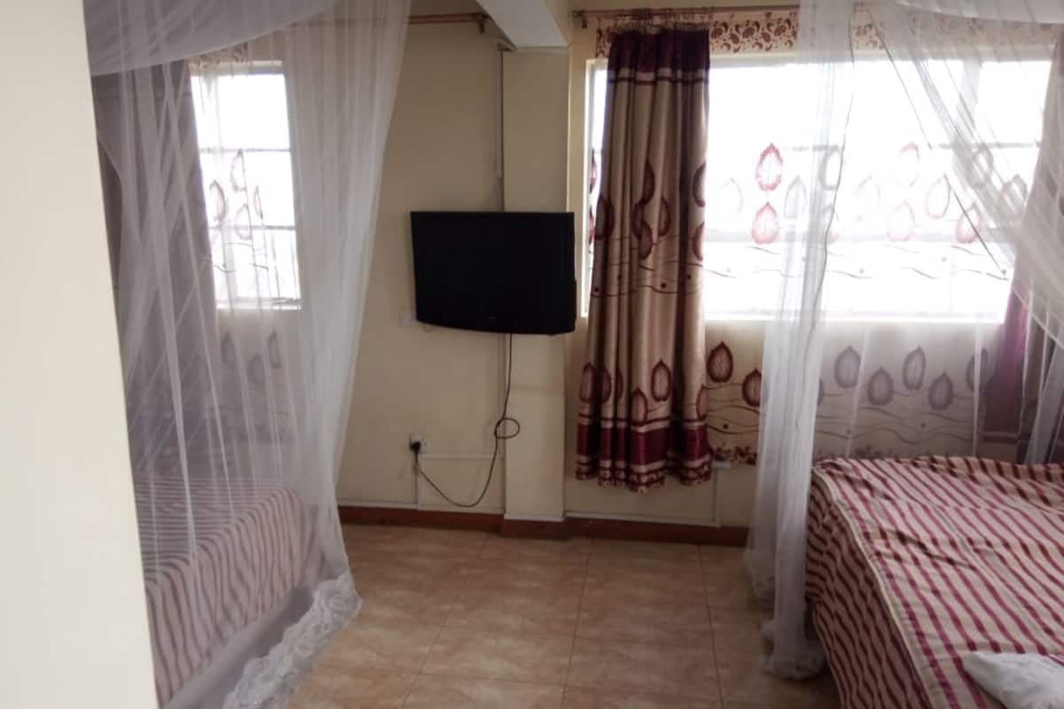 Un dormitorio con cama, televisor montado en la pared y ventana con cortinas.