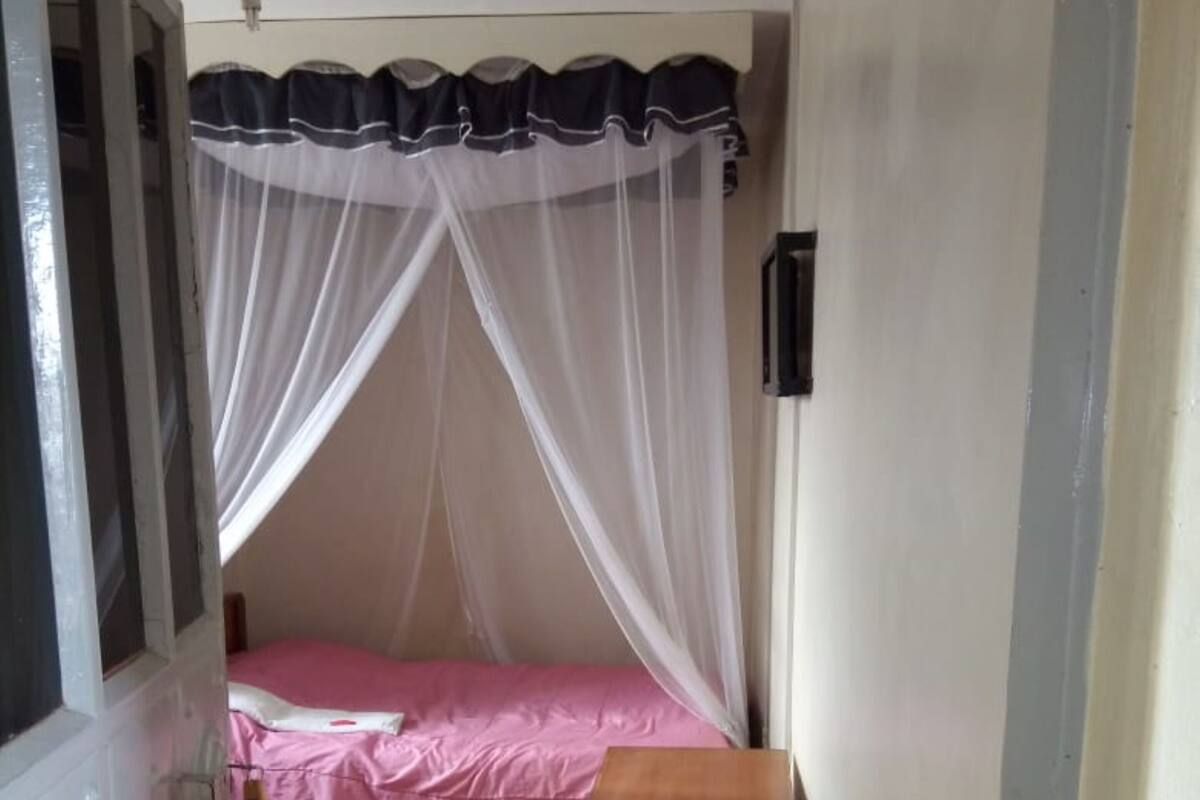 Una habitación estrecha con una cama, una cesta azul y una pared blanca.