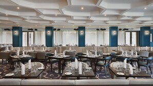 A spacious dining area with multiple tables set for service, a high ceiling with geometric patterns, and large windows with curtains. - Buxton Crescent (Buxton)